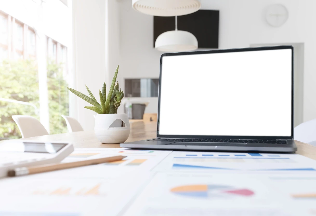Laptop with a blank screen beside printed data charts and reports on a desk